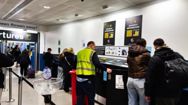 Пасажири шикуються в чергу на контрольно-пропускному пункті в аеропорту Манчестера поруч зі співробітниками в жилетах високої видимості.