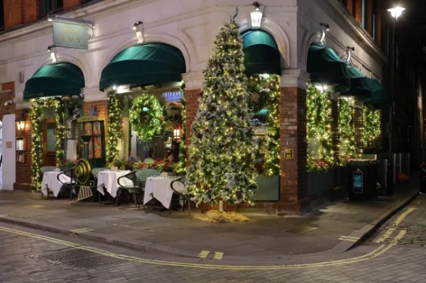 Лондон, Велика Британія – 17 листопада 2025 року: Ресторан Ivy на Мерілебон-лейн сяє багатою різдвяною зеленню та високою святковою ялинкою, що освітлює тихий вечірній вуличний куточок.; Shutterstock ID 2711751015; замовлення_на_продаж: -; робота: -; клієнт: -; інше: