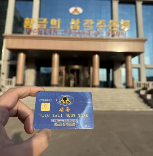 Синю банківську картку тримають у руці перед банком та сходами, що ведуть до неї в Північній Кореї.