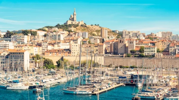 Яскравий вид на історичний порт Марселя, з човнами, що стоять на воді перед Марсельською цитаделлю, та собором Паризької Богоматері на вершині пагорба.