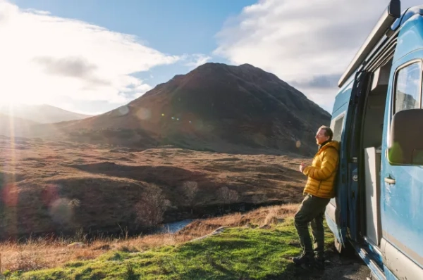 Зрілий чоловік милується краєвидом Шотландського нагір'я сонячного зимового дня зі свого кемпера.