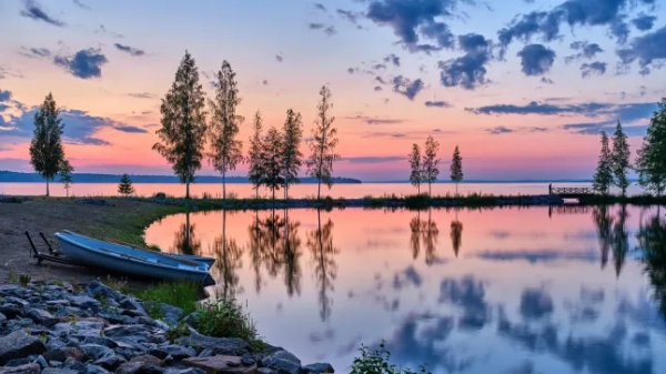 Озеро в Тампере, Фінляндія, на світанку. Рожево-фіолетове небо з темними хмарами та високими деревами відбивається у воді.