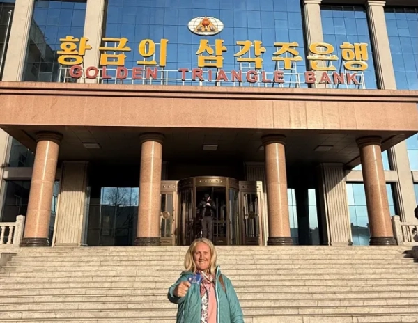 Джанет Ньюенхем у синій куртці та джинсах тримає банківську картку біля банку в Північній Кореї.