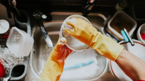 Крупний план рук людини в жовтих рукавичках, яка миє посуд на кухні.