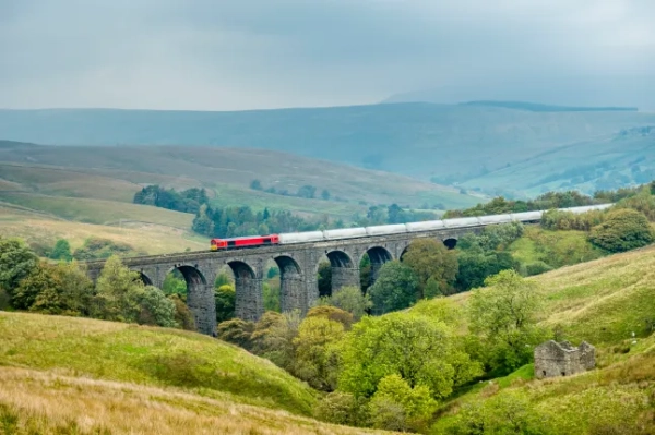 Поїзд у Йоркширських долинах проїжджає віадук Дент-Хед, арочний міст над зеленими полями та деревами.