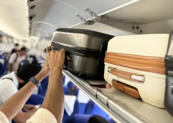 Зображення невпізнаного чоловіка, який кладе сіру валізу на колесах у багажне відділення салону літака, фокус на передньому плані