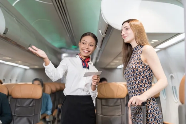 Стюардеса та пасажир у літаку. Стюардеса зустрічає пасажирів та перевіряє пасажирські квитки в салоні літака. Жінка-стюардеса допомагає та обслуговує пасажирів у літаку.