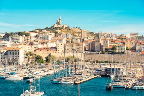 Яскравий вид на історичний порт Марселя, з човнами, що стоять на воді перед Марсельською цитаделлю, та собором Паризької Богоматері на вершині пагорба.