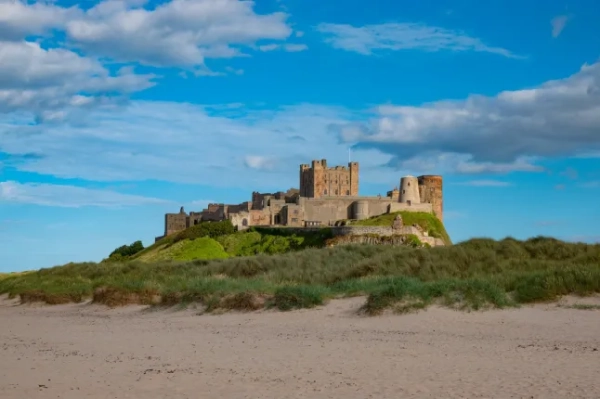 ЗАМОК БАМБУРГ, НОРТУМБЕРЛЕНД, АНГЛІЯ, ВЕЛИКА БРИТАНІЯ, 15 ВЕРЕСНЯ 2023 РОКУ: Замок Бамбург над піщаним пляжем у сонячному Нортумберленді. Приголомшливий прибережний краєвид зі знаменитою фортецею на березі Північного моря.