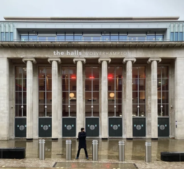 Бен Ейткен стоїть у чорній куртці біля музичного майданчика Halls у Вулвергемптоні дощового дня.