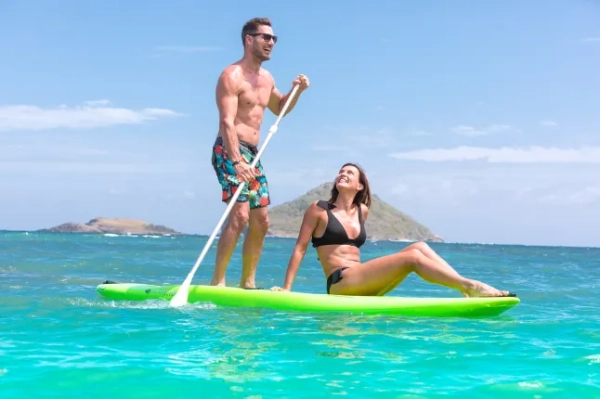Чоловік і жінка на дошці для веслування в океані. Чоловік стоїть і керує дошкою, жінка сидить і повертається, щоб подивитися на нього.