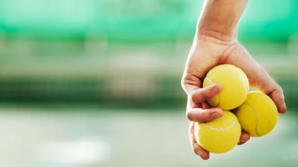 Молодий чоловік тримає в руці три тенісні м'ячі.