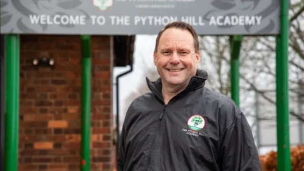 Енді Стірленд посміхається перед вивіскою Академії Пайтон-Гілл.