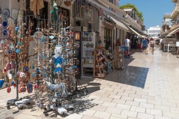 Сувенірний магазин, що продає прикраси ручної роботи, та туристи, що йдуть вулицею в Греції