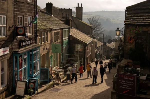 Громадськість прогулюється головною вулицею в центрі села Хаворт, північна Англія, 25 лютого 2026 року. Розташований на краю Пеннінських вересових пустищ, Хаворт всесвітньо відомий своїм зв'язком із сестрами Бронте, які написали свої відомі літературні твори, живучи в пасторському будинку Хаворт. «Грозовий перевал», запальна екранізація британського режисера Емеральд Феннелл класичного роману Емілі Бронте, у головних ролях якої Марго Роббі та Джейкоб Елорді грали приречених закоханих Кеті та Хіткліффа, очолив касові збори після виходу в середині лютого. (Фото Олі СКАРФФ / AFP via Getty Images)