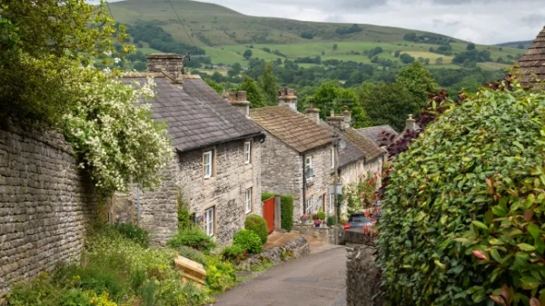 Чарівна вулиця з кам'яними будинками в Каслтоні, в долині Надії в Пік-Дистрикті, оточена зеленню, полями та пагорбами за будинками.