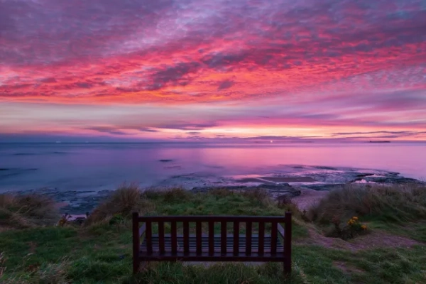 Пляж Бамбург з лавкою на світанку з червоним та рожевим небом. Нортумберленд. Велика Британія.