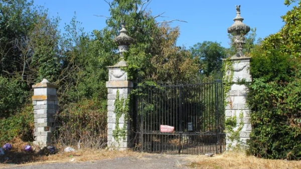 Величні залізні ворота біля Стенвелл-Плейс з кам'яними скульптурами з обох боків. Вони зарослі, а спереду прикріплений червоний знак з написом «Вхід заборонено».
