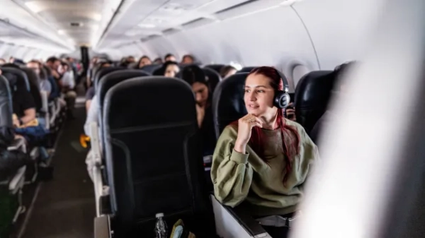 Молода жінка з бездротовими навушниками-вкладишами сидить у переповненому літаку.