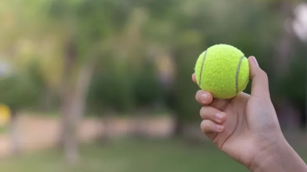 Крупний план руки, що тримає тенісний м'яч надворі.
