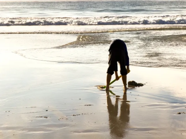 Кавказький хлопчик копає яму лопатою в піску на пляжі