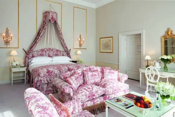 Номер Junior Suite у The Merrion. Ліжко в історичному стилі з вишуканим балдахіном, перед ним — диван у рожево-білу квітку.