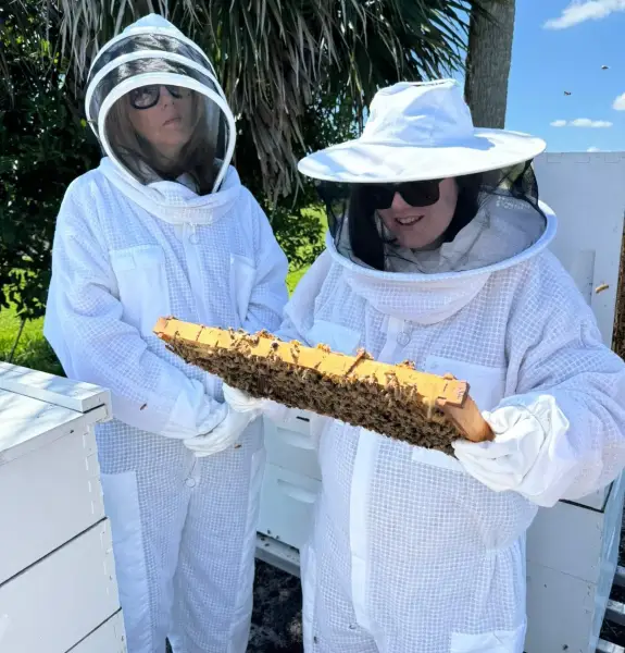 Alex Goldsmith and a guide in beekeeping suits. Alex is holding a giant piece of honeycomb.
