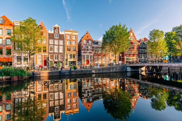 A canal and row of waterside houses in Amsterdam around sunset, with trees and warm light.