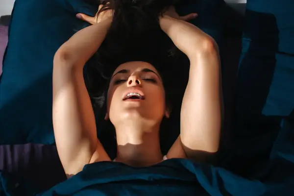 Young woman in bed with her arms by her head