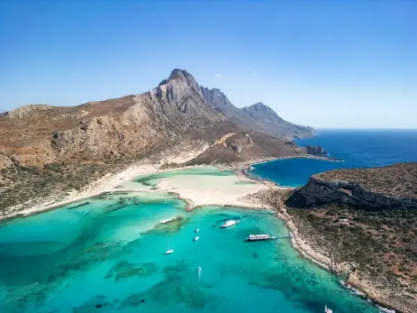 An aerial view of the Greek island of Crete, with cliffs, white sand beaches, and turquoise and dark blue sea.