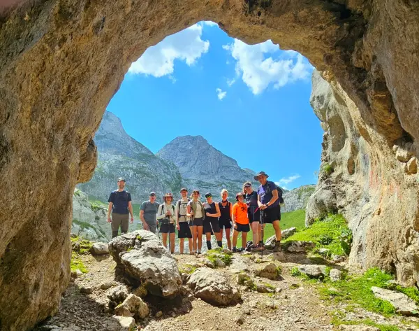 Албанські Альпи: де пиво коштує менше долара 11 A group of hikers standing in the mouth of a cave in the Albanian Alps with mountains in the background. The sky is bright blue.