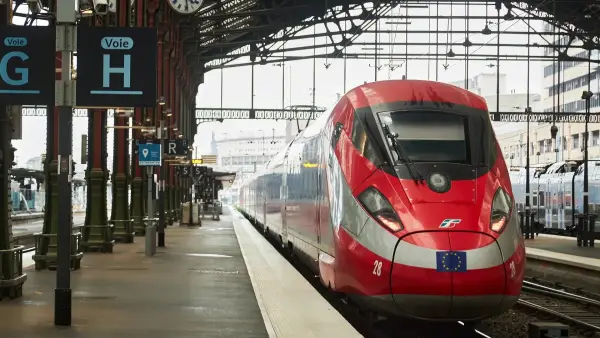 A red FS Group train sitting at a station platform.