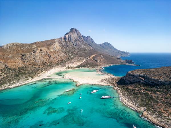 An aerial view of the Greek island of Crete, with cliffs, white sand beaches, and turquoise and dark blue sea.