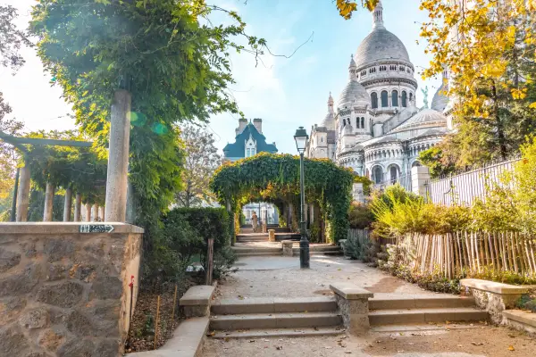 The tall monument of Sacre Coeur from romantic public park with vegetation tunnel created with the botany plants of the park.