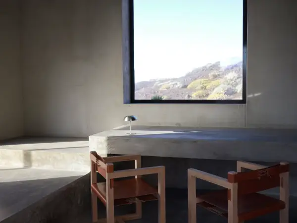 A room at El Elevador, with grey walls, a bare table, two chairs sat next to it, and a window with a view of the island.