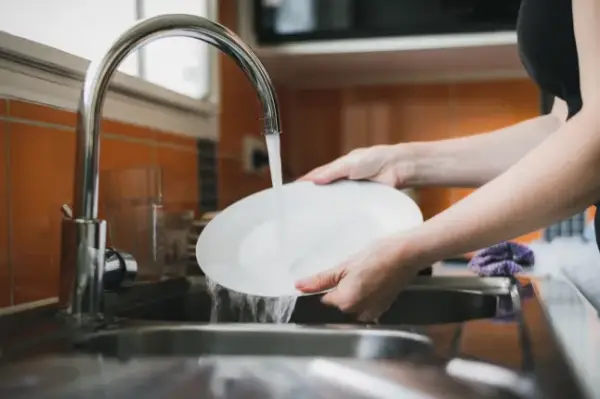 Woman washing dishes in kitchen sink, close up of hands rinsing plate.; Shutterstock ID 2226844453; purchase_order: -; job: -; client: -; other: -