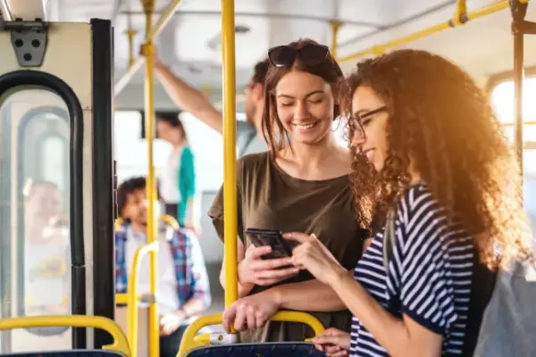 Two friends looking in phone while standing on a bus.; Shutterstock ID 1378340717; purchase_order: -; job: -; client: -; other: -