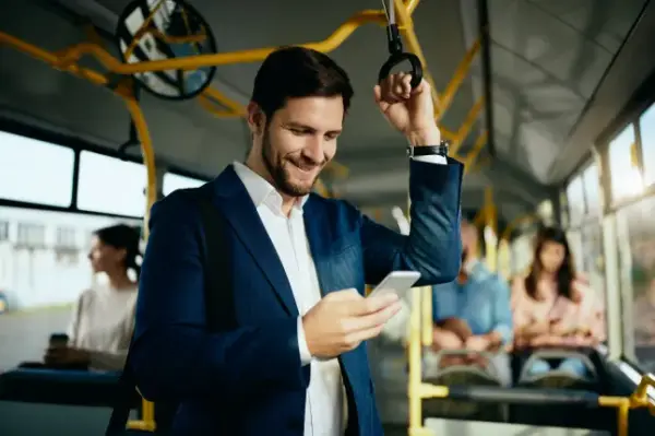 Happy male entrepreneur using mobile phone and text messaging while commuting by public bus.; Shutterstock ID 1897733494; purchase_order: -; job: -; client: -; other: -