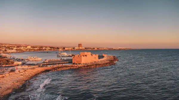Scenic view of Paphos Castle and harbor at sunset, with boats and a calm sea, capturing the historic charm and beauty of Cyprus.